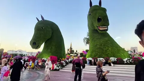 Two gigantic topiary horse heads towering above a plaza filled with admiring tourists.