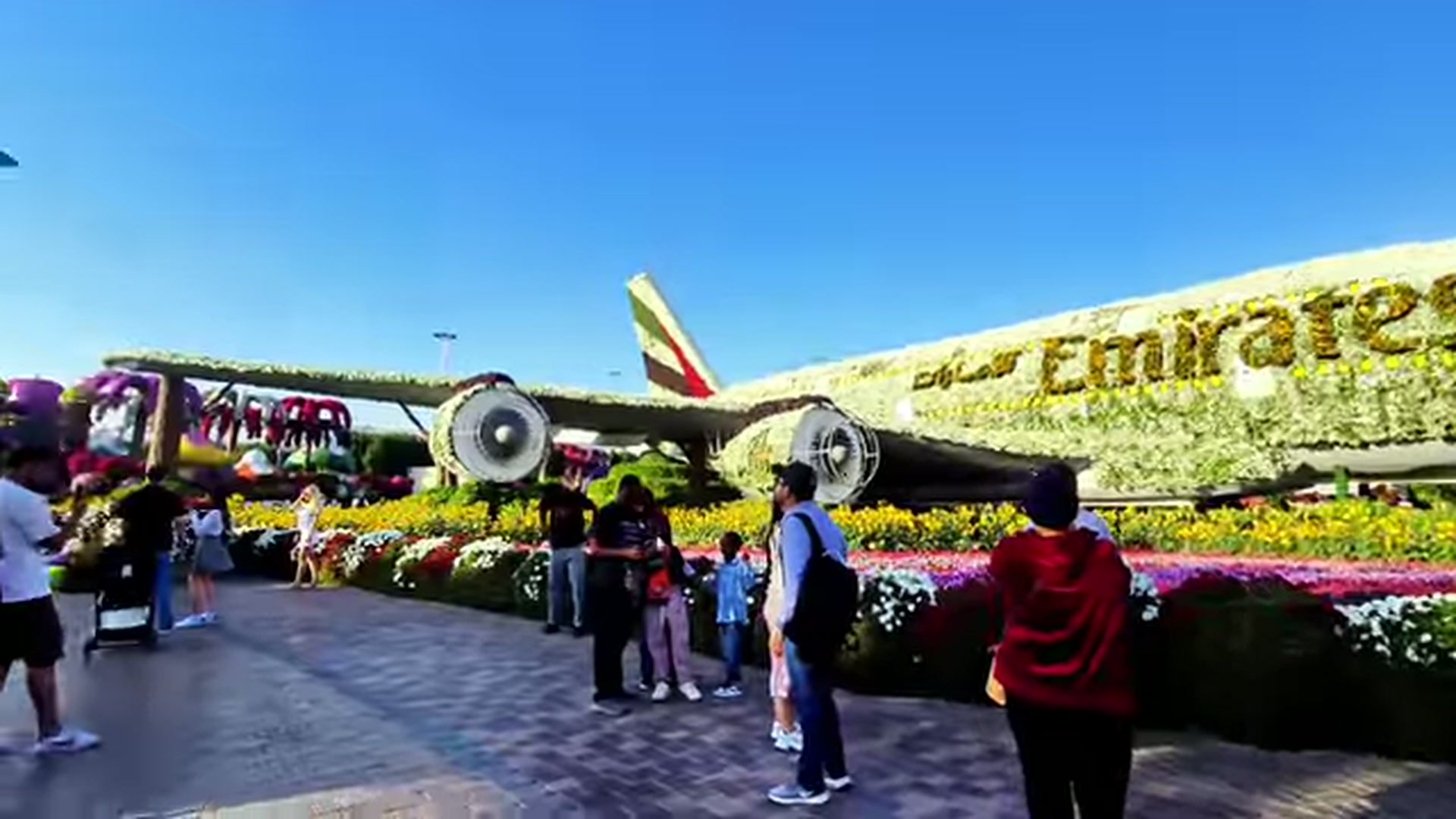 A massive life-sized Emirates A380 airplane completely covered in flowers with tourists taking photos in front of it.