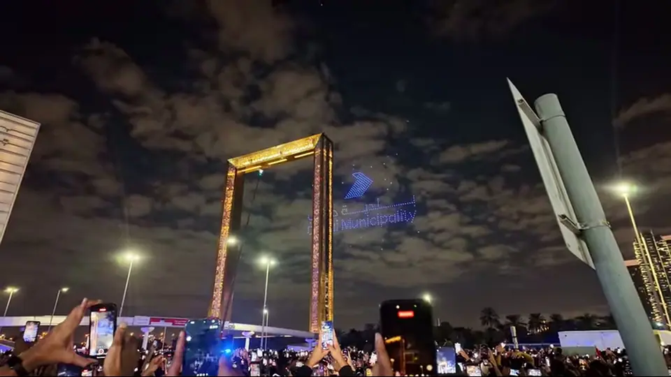 Wide night view of Dubai Frame with crowd, haze and skyline.