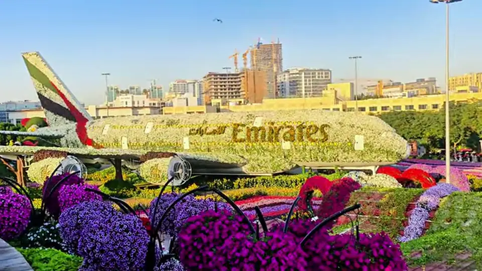 Emirates floral airplane display among flower beds and distant buildings.