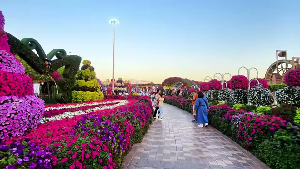 Symmetrical flower-lined path with butterfly topiary in evening light.