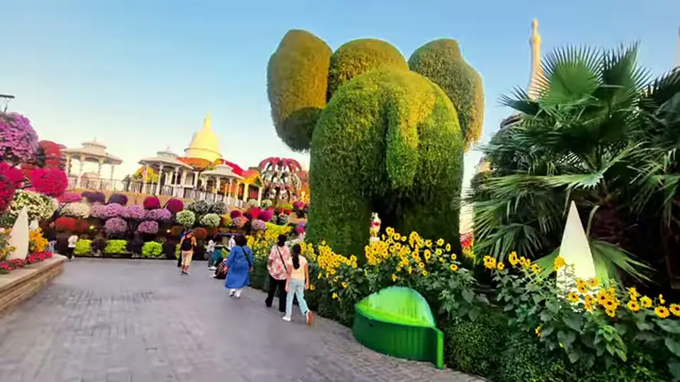 Giant green elephant topiary beside a path with yellow flowers.