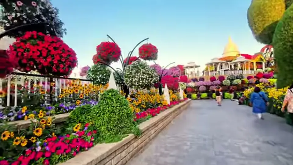 Garden pathway bordered by bright flowers and hanging floral spheres.