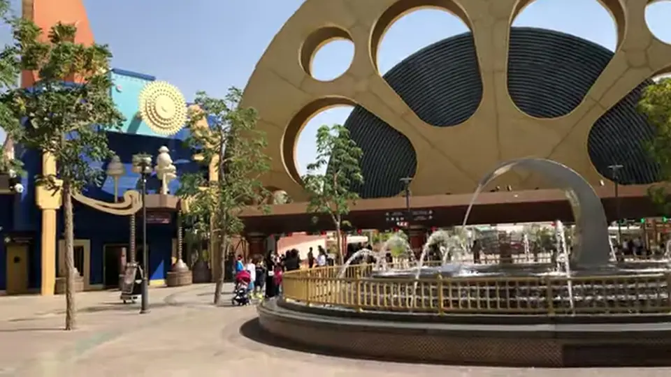 Fountain plaza facing a giant film-reel arch in daylight.