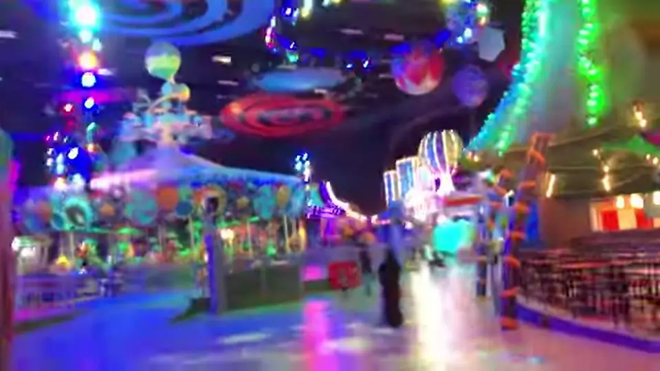 Indoor carnival with glowing facades, balloons, and candy-like rides.