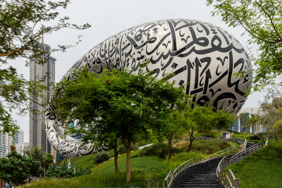 Futuristic building with Arabic calligraphy, surrounded by lush greenery and modern skyscrapers in the background.
