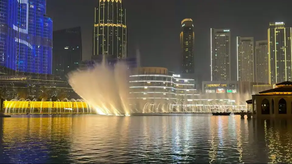 Бурдж-Халифа сияет синим над озером, отражения и skyline ночью.