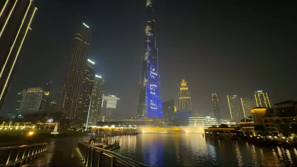 Белая скульптура руки снизу вверх на фоне освещенных башен ночью.