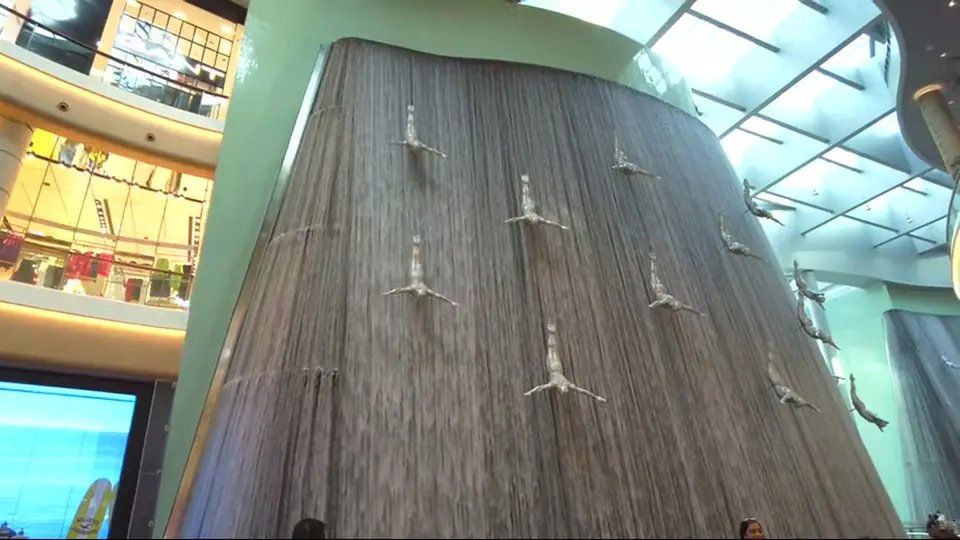 Ярко освещенные высокие струи фонтана, лодка силуэтом у края ночью.