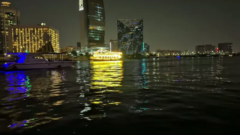 Night view across Dubai Creek with illuminated boat and skyline reflections