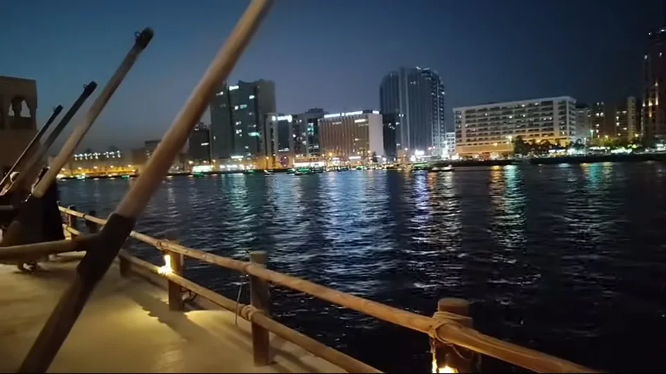 Night view across Dubai Creek from a wooden boat with city lights reflecting on the water