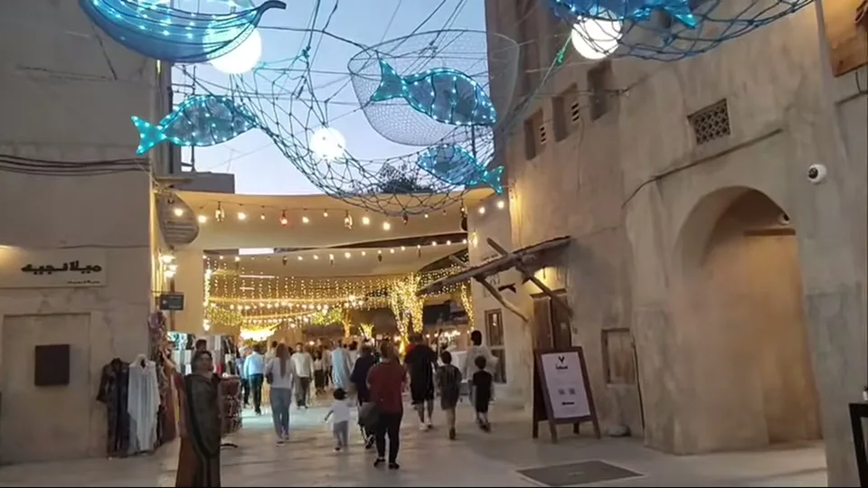 Crowded heritage alley in Dubai with glowing fish lights overhead at dusk