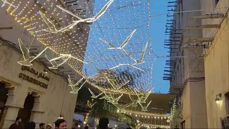Glowing bird lights suspended above a lively evening alley in Al Seef