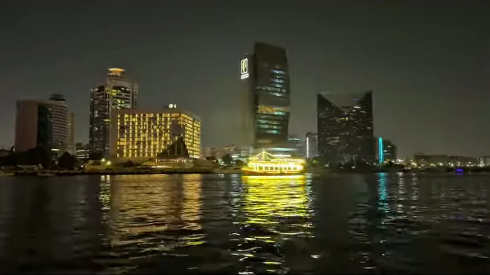 Dubai Creek skyline at night with a glowing boat crossing the water