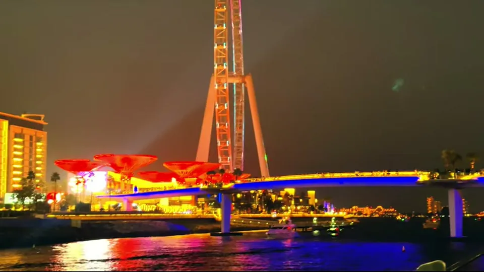 Illuminated bridge and Ain Dubai base reflected on water at night