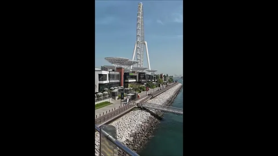 Ain Dubai rising above Bluewaters waterfront and seawall beside a turquoise channel
